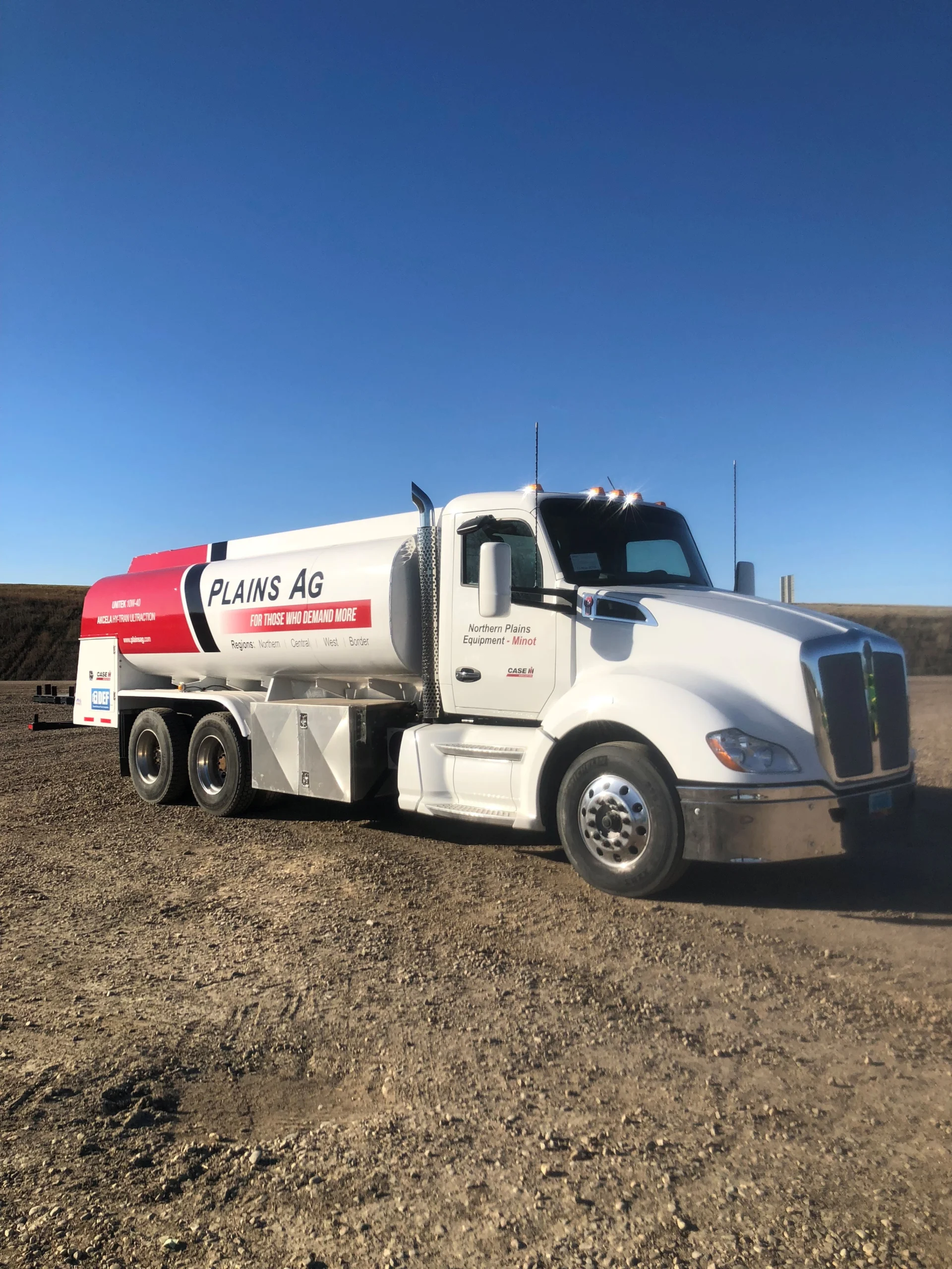 A white and red Plains Ag fuel delivery truck is parked on a gravel surface in an open, rural area under a clear blue sky, representing Fuel System Installation & Repair in Minnesota.
